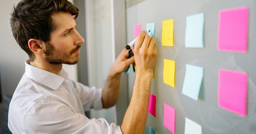 Focused businessman writing on sticky notes in a modern office environment.