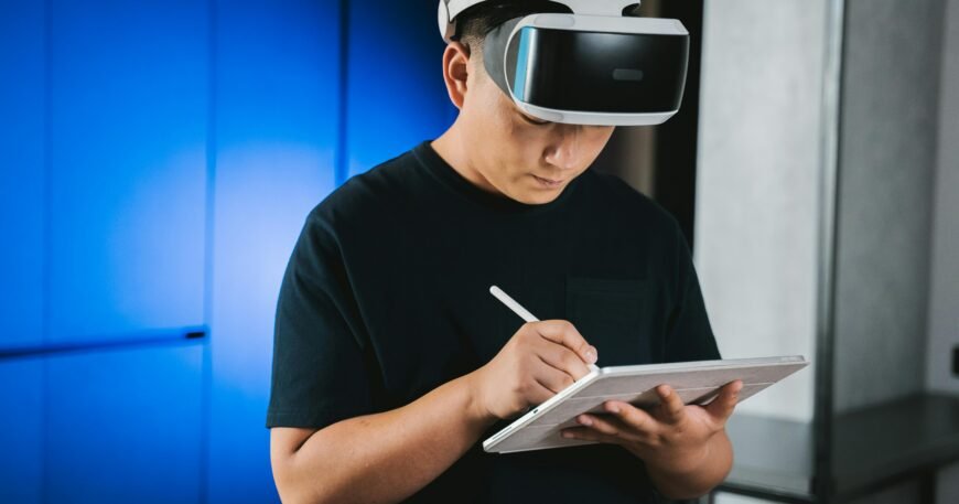 A man indoors wearing a VR headset while writing on a tablet with a stylus pen.